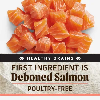 A close-up of diced raw salmon bites on a white background. Text below reads "Grain free. First ingredient is deboned salmon. Poultry free"