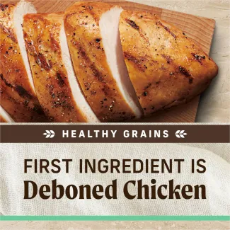 A topdown photo of cooked sliced chicken on a wooden serving board; text below reads "healthy grains. First ingredient is deboned chicken"