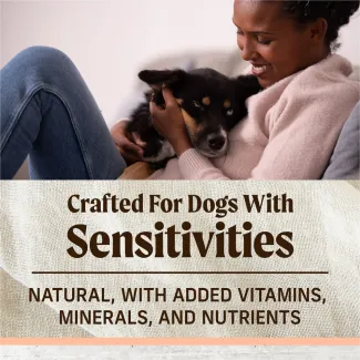 The top of the image shows a woman sitting on the couch snuggling a black and tan dog; text below reads "crafted for dogs with sensitivities. Natural with added vitamins, minerals, and nutrients" 